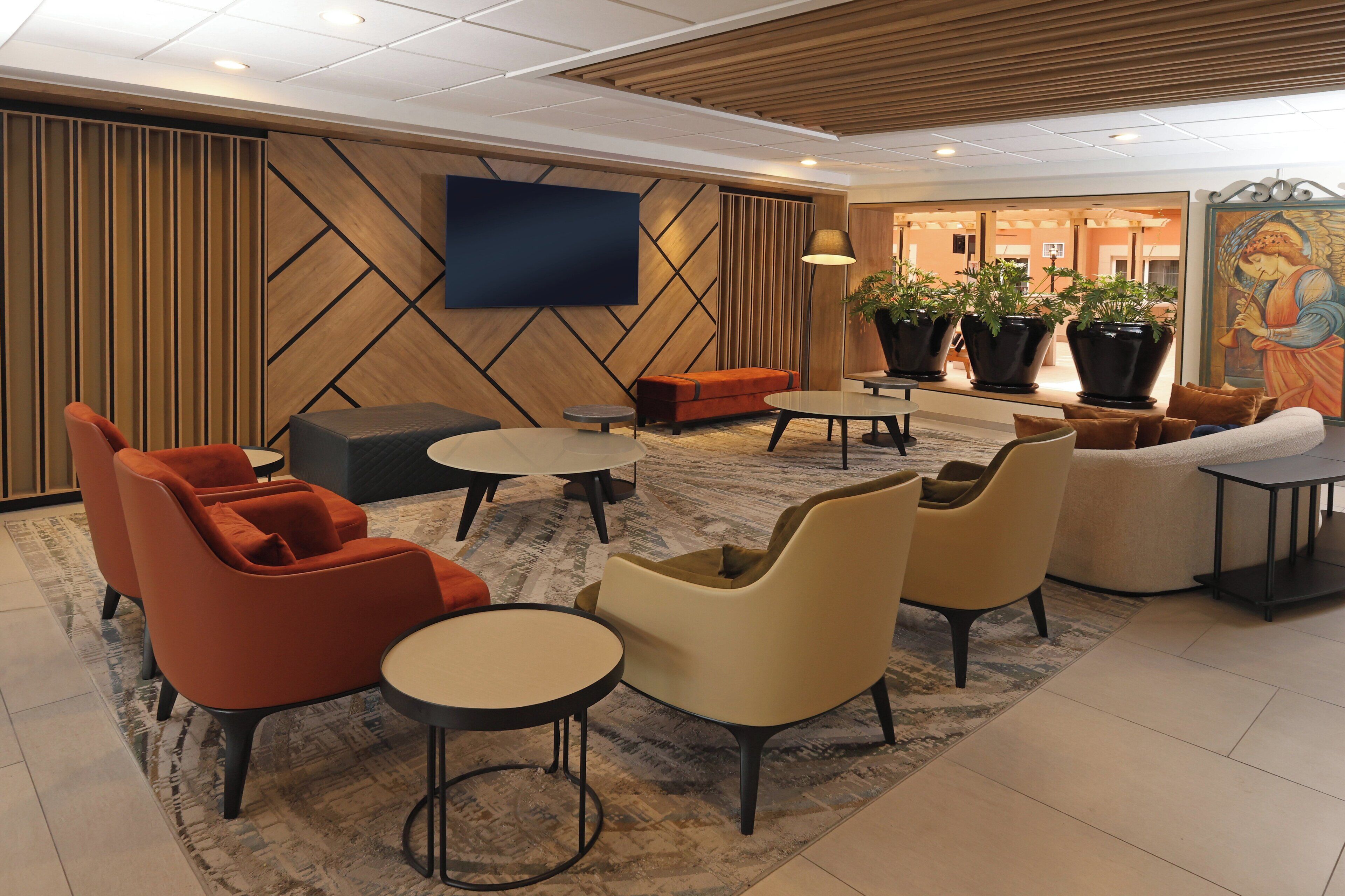A modern lobby with seating areas, a flat-screen TV, and potted plants.