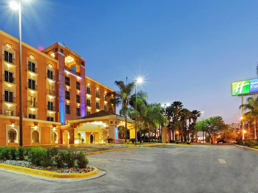 A hotel with multiple floors, a well-lit entrance, and a parking area with palm trees.