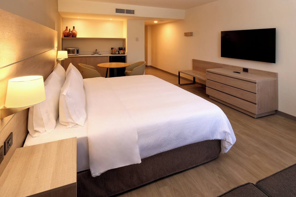 Una habitación de hotel con cama, escritorio, silla, televisión y kitchenette.