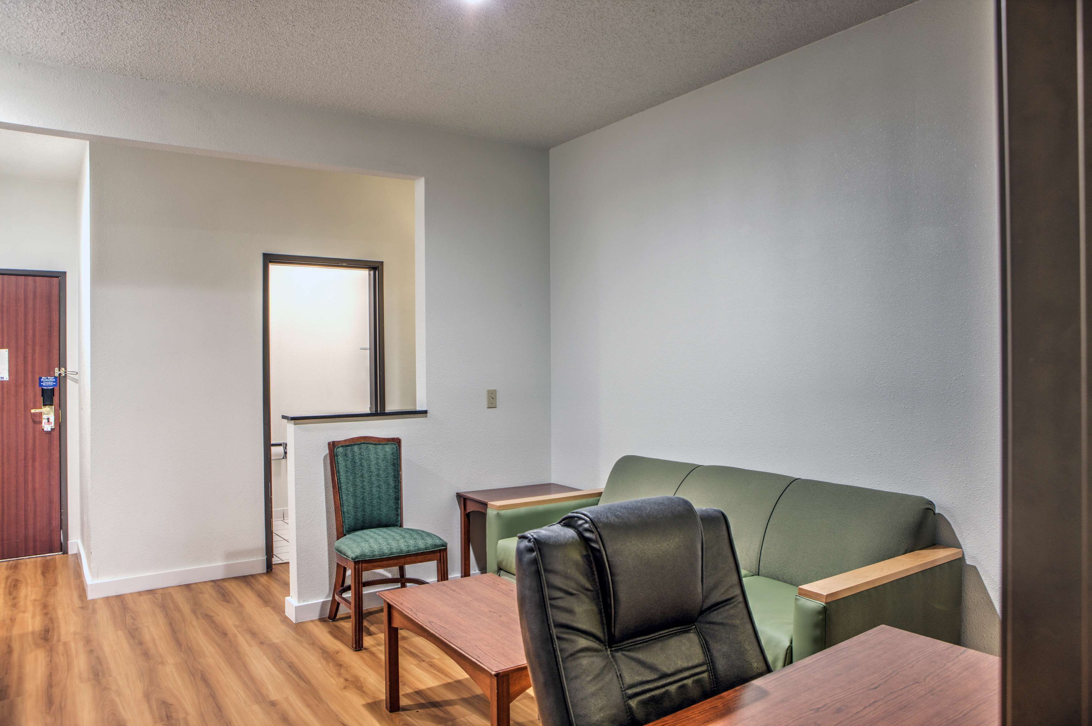 Una habitación con un sofá verde, una mesa de madera, una silla verde y un escritorio de madera.