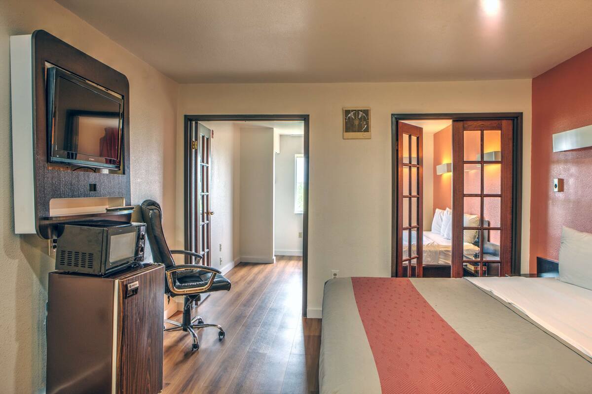 A hotel room with a bed, a desk with a computer, a chair, a TV, and a microwave.