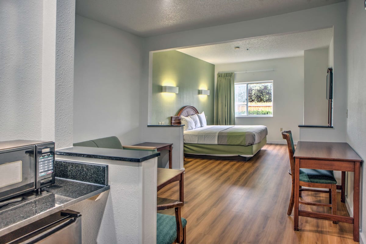 A hotel room with a bed, a desk with a computer, a chair, and a microwave.