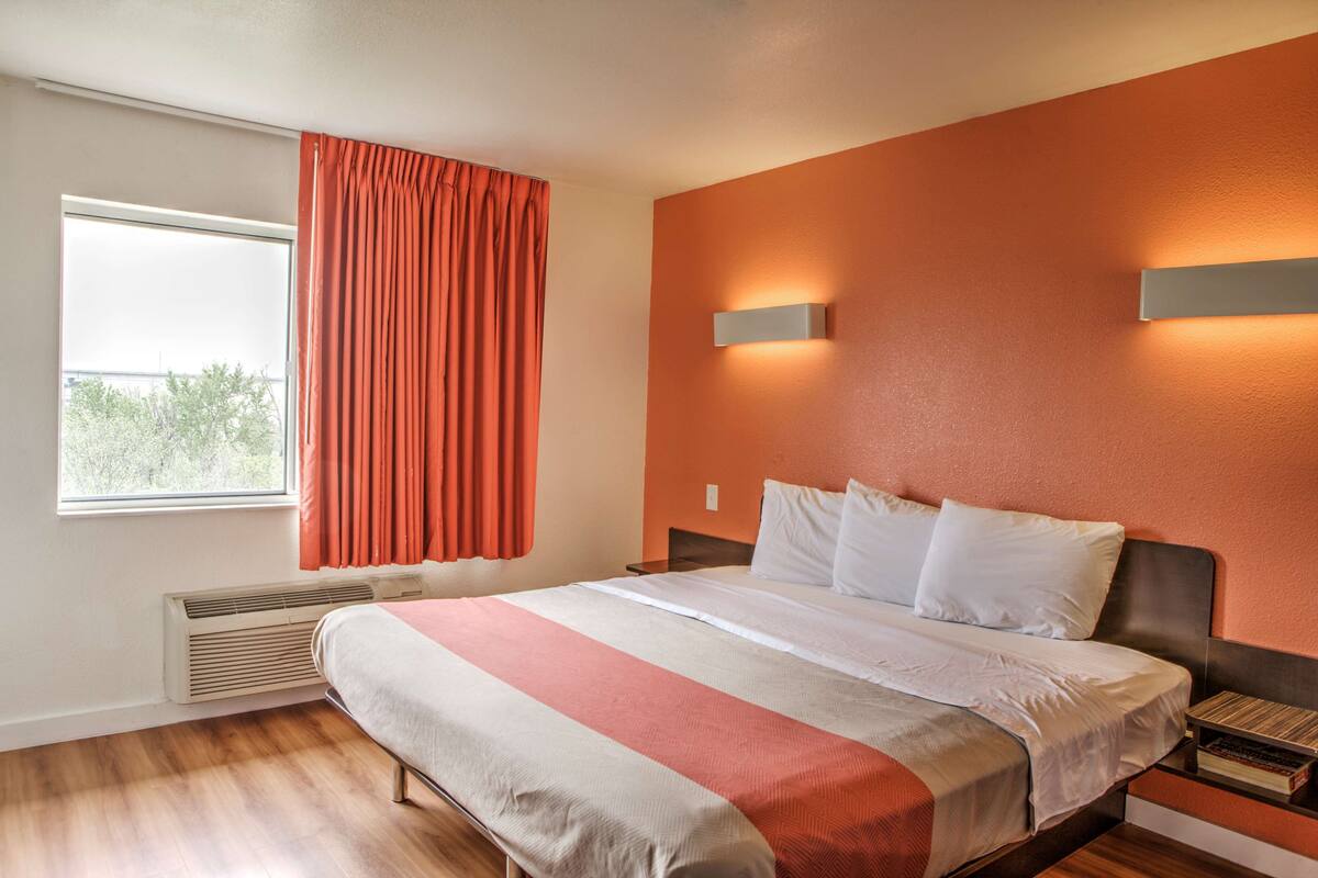 A hotel room with a large bed, a window with curtains, a wall-mounted light, and a radiator.