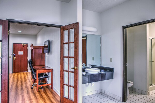 A hotel room with a wooden desk, a chair, a large mirror, a sink, and a toilet.