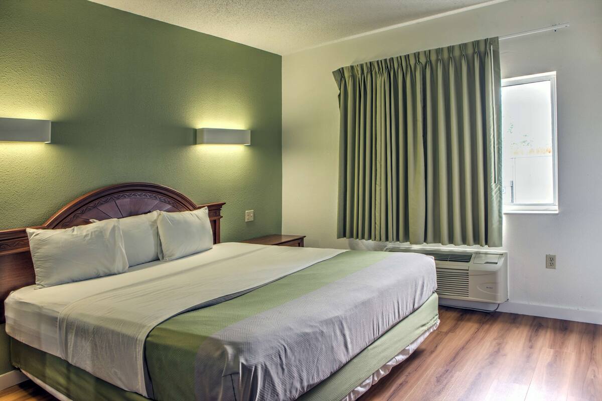 A neatly made bed with a wooden headboard, a bedside table, and a wall-mounted light fixture.
