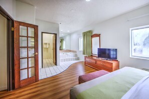 A hotel room with a wooden floor, a bed, a TV, a dresser, a window with a view, and a bathroom with a bathtub and toilet. - Motel 6 Dallas, TX - Northwest (Dallas)