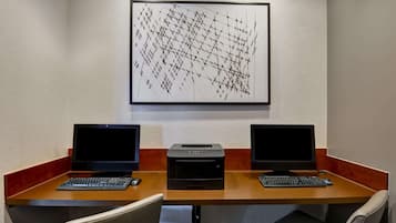 Uma sala de conferências com duas mesas, cada uma com um laptop e uma impressora. Há duas cadeiras e um quadro abstrato grande na parede.