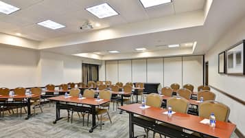 A conference room with multiple tables and chairs, equipped with water bottles, a projector, and a screen.