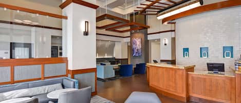 A modern hotel lobby with seating areas, a reception desk, and a large screen.