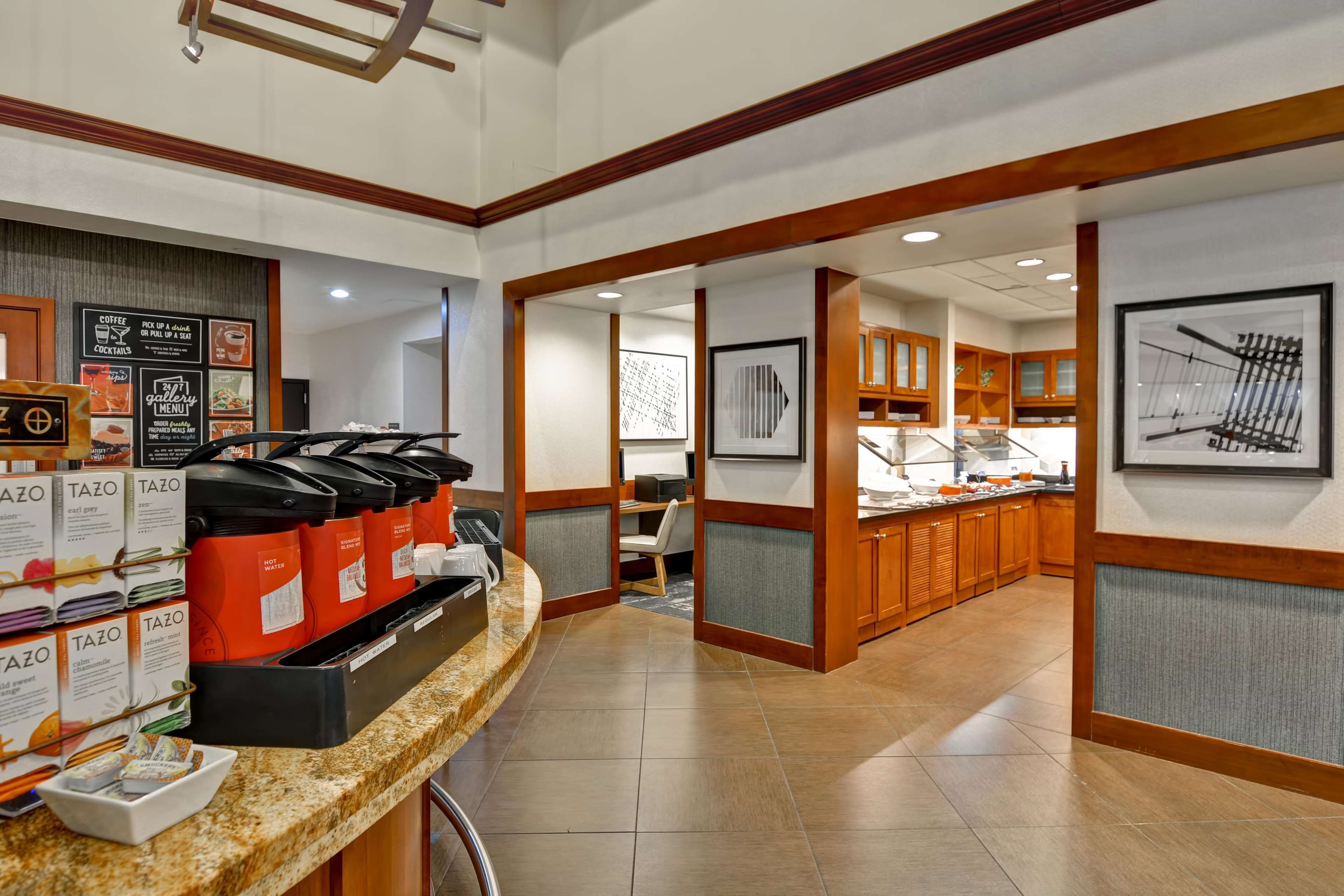 A hotel lobby with a coffee station, a reception desk, and a dining area with wooden cabinets.