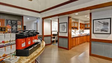 A hotel lobby with a coffee station, a reception desk, and a dining area with wooden cabinets.