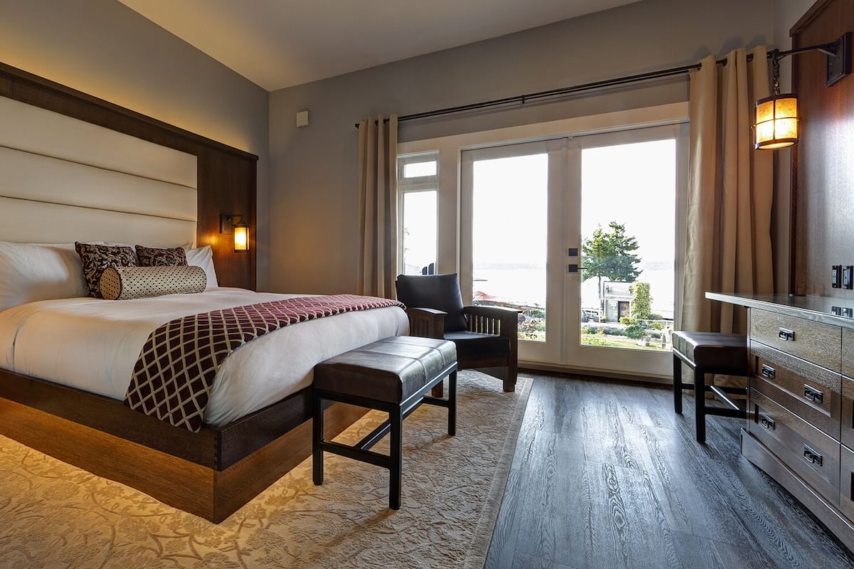 Ein Hotelzimmer mit einem großen Bett, einem Schreibtisch, einem Stuhl und Blick ins Freie.