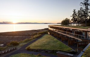 A modern building with a glass balcony overlooking a beach and water.