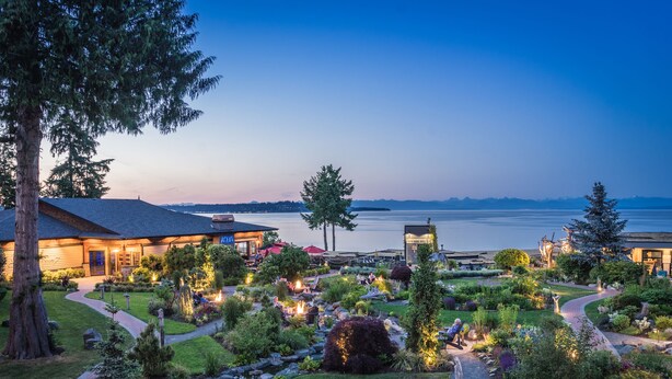 A landscaped garden with pathways, a building with a red umbrella, and a view of the water. - Kingfisher Pacific Resort and Spa (Courtenay)