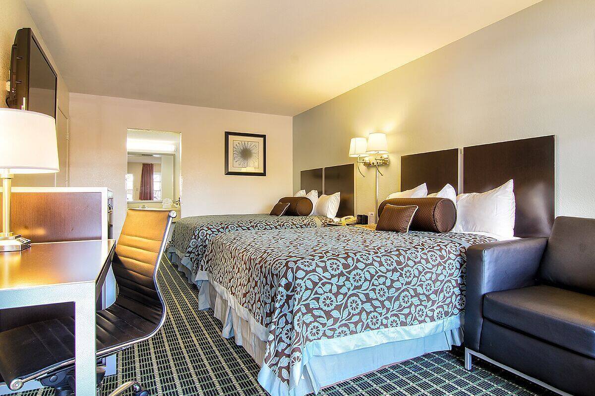 A hotel room with a bed, a desk, a chair, a sofa, a lamp, and a mirror.