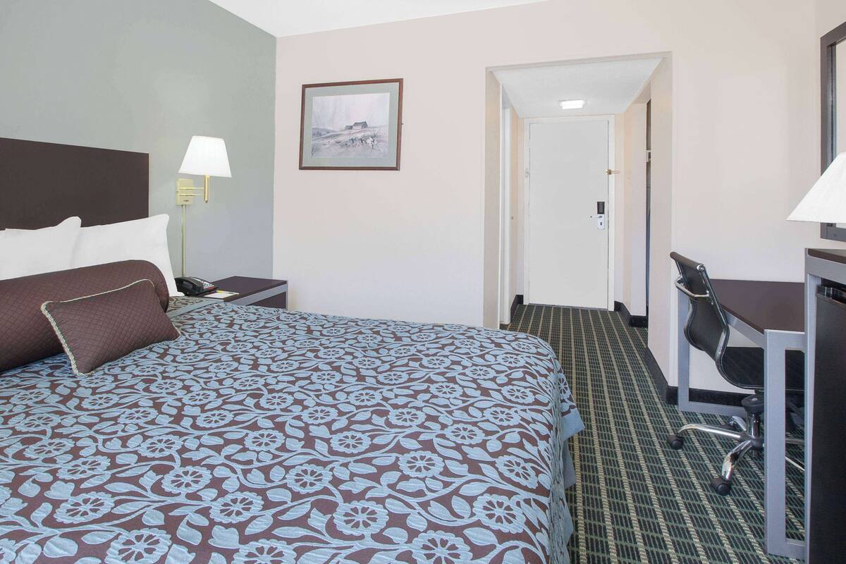A hotel room with a large bed, a desk, a chair, and a picture on the wall.