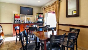 A dining area with a table and chairs, a television, a refrigerator, and a vending machine. - Days Inn by Wyndham Market Center Dallas Love Field (Dallas)