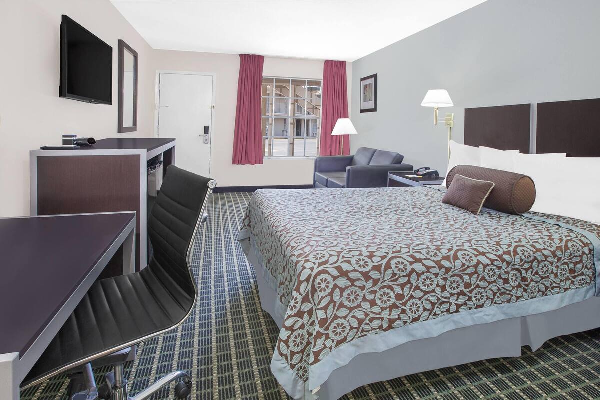 A hotel room with a bed, a desk, a chair, a TV, and a window with curtains.