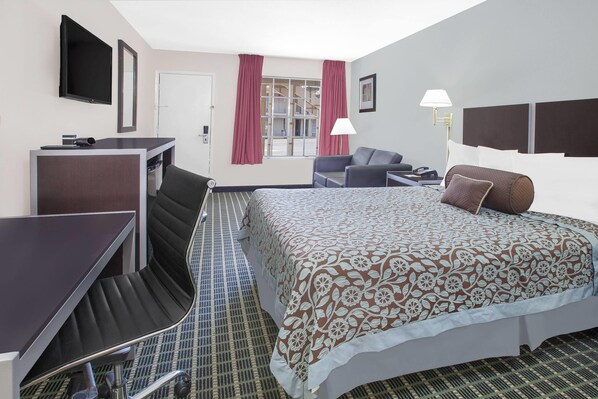 Une chambre d’hôtel avec un lit, un bureau, une chaise, une télévision et une fenêtre avec des rideaux.