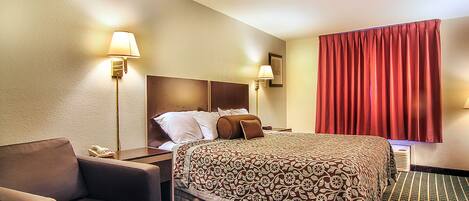 Quarto de hotel com uma cama grande, duas luminárias de cabeceira, uma cabeceira, uma cortina vermelha e um tapete estampado.