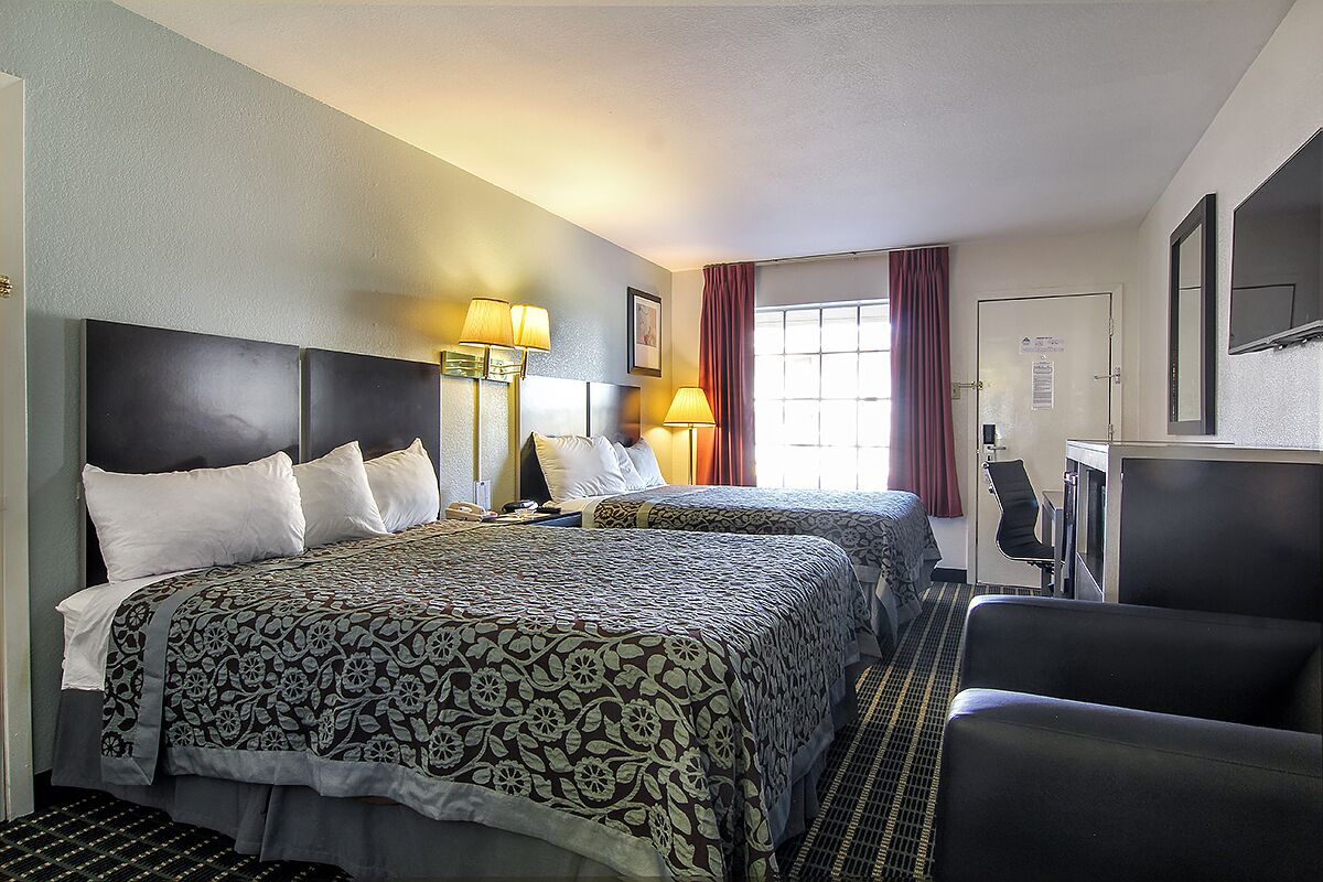 Une chambre d’hôtel avec deux lits, un bureau, une chaise et un téléviseur.