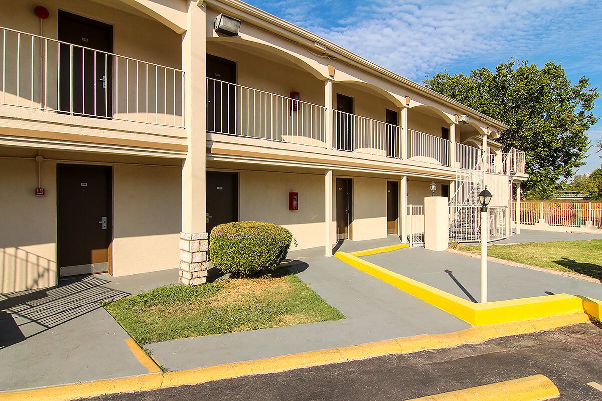 A two-story motel with a flat roof, balconies, and a small lawn area.