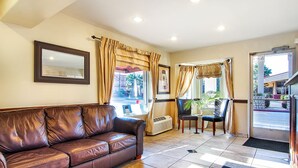 A hotel lobby with a leather sofa, two chairs, a large mirror, and a door leading outside. - Days Inn by Wyndham Market Center Dallas Love Field (Dallas)