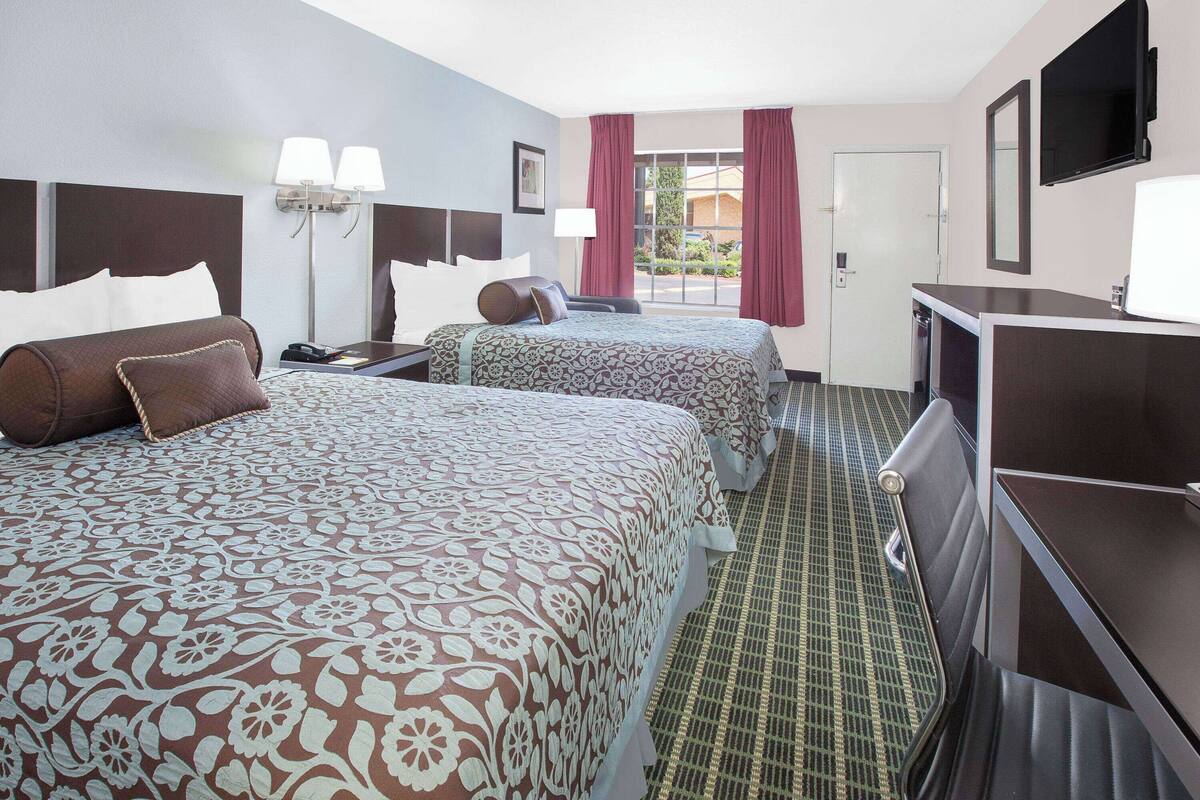 A hotel room with two beds, a desk, a chair, a TV, and a window with curtains.