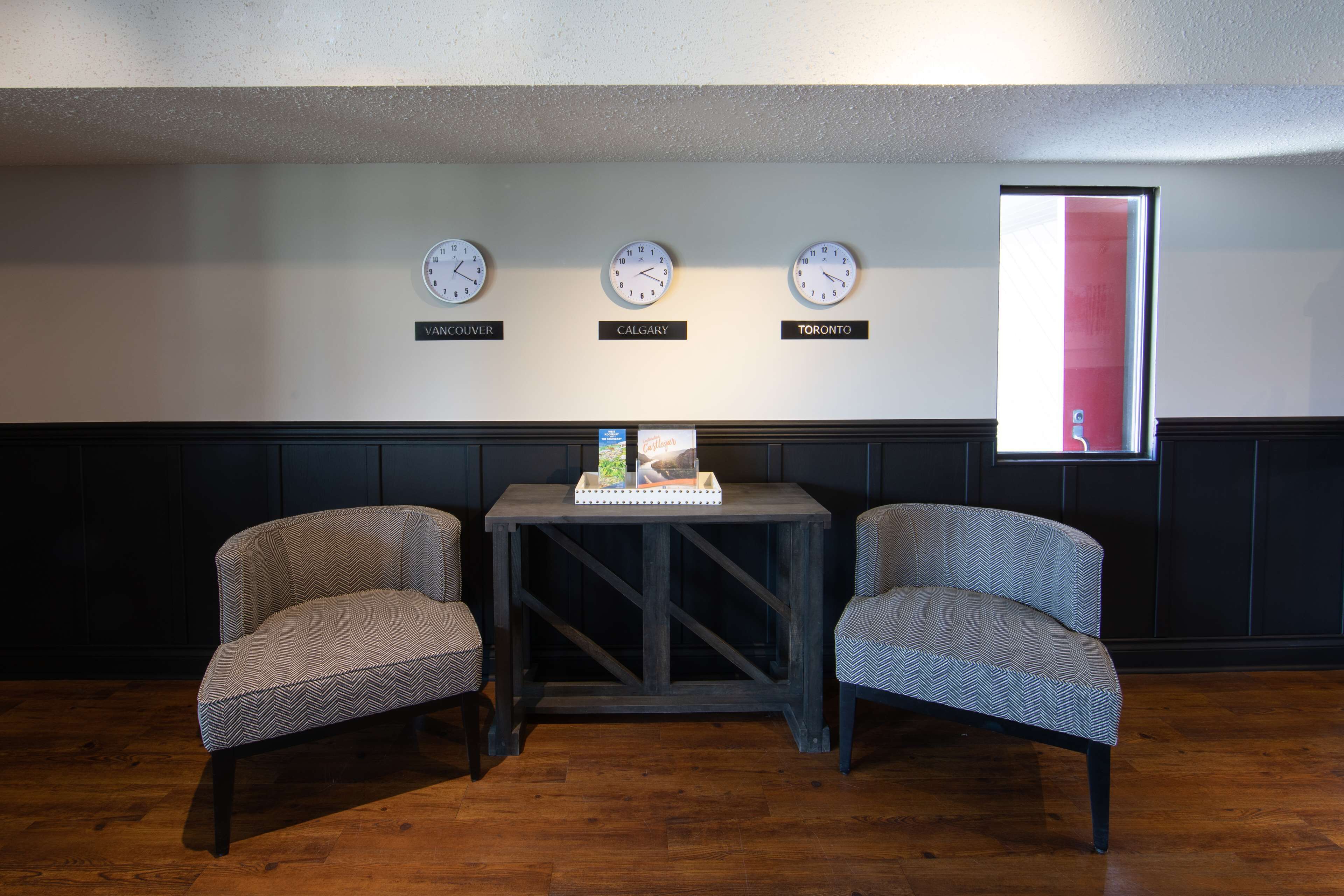 Une pièce comprenant deux fauteuils, une petite table ornée d’un objet décoratif et trois horloges indiquant le nom de différentes villes.