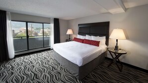 Una habitación de hotel con una cama grande, dos mesitas de noche con lámparas, una alfombra con estampado de cebra y vistas al exterior a través de un ventanal.