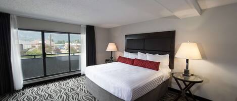 Une chambre d’hôtel avec un grand lit, deux tables de chevet avec des lampes, un tapis à motifs zébrés et une vue sur l’extérieur grâce à une grande fenêtre.