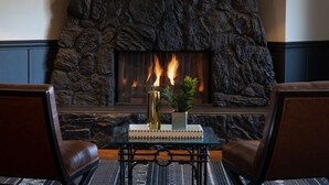 Una chimenea de piedra con fuego, dos sillones de cuero, una mesa de vidrio con adornos y una planta en maceta.