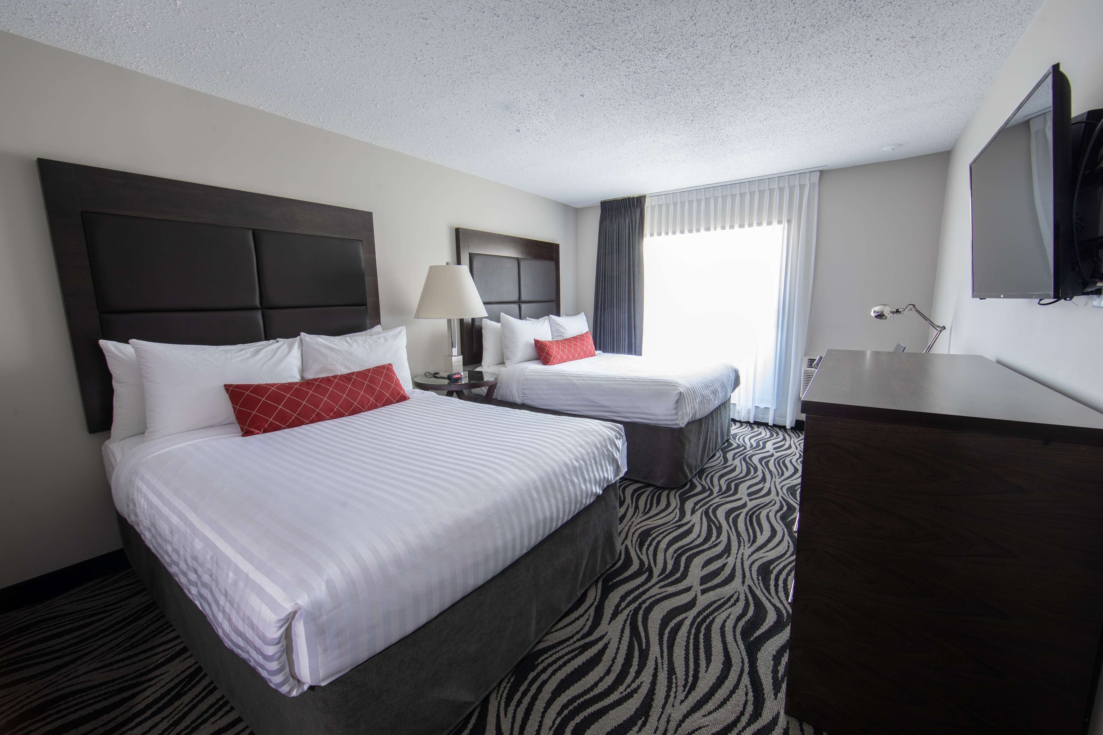 A hotel room with two beds, a large flat-screen TV, a desk, and a zebra-patterned carpet.
