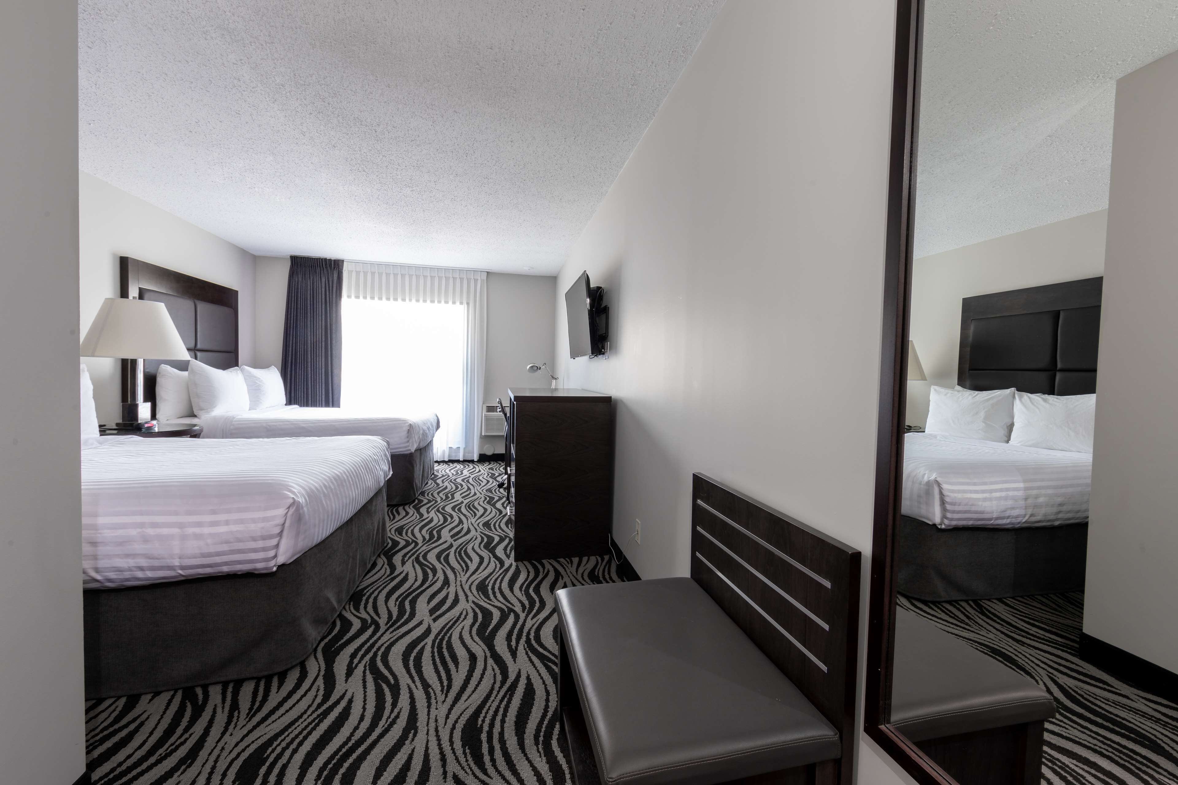 A hotel room with two beds, a bench, a desk, a mirror, and a zebra-patterned carpet.