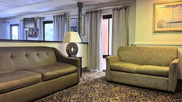 A room with a sofa, a chair, a lamp, a patterned carpet, and a painting on the wall.