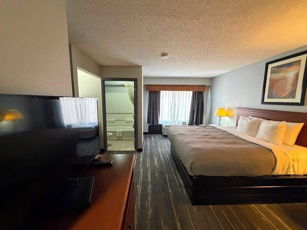 Habitación de hotel con cama, televisión, escritorio y ventana con cortinas.