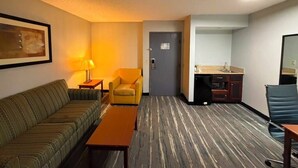 Une chambre d’hôtel équipée d’un canapé, d’un fauteuil, d’un bureau et d’une petite kitchenette.