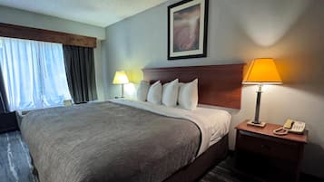 A hotel room with a large bed, two bedside lamps, a telephone, and a painting on the wall.