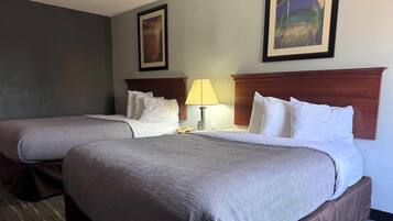 Habitación de hotel con dos camas, una mesita de noche con lámpara y dos cuadros en la pared.