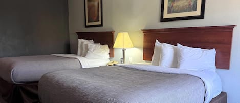 A hotel room with two beds, a nightstand with a lamp, and two framed pictures on the wall.