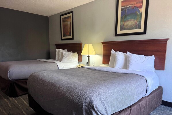 Habitación de hotel con dos camas, una mesita de noche con lámpara y dos cuadros en la pared.