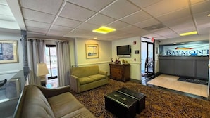 Un hall d’hôtel avec un canapé, une table basse, un téléviseur et un comptoir de réception.
