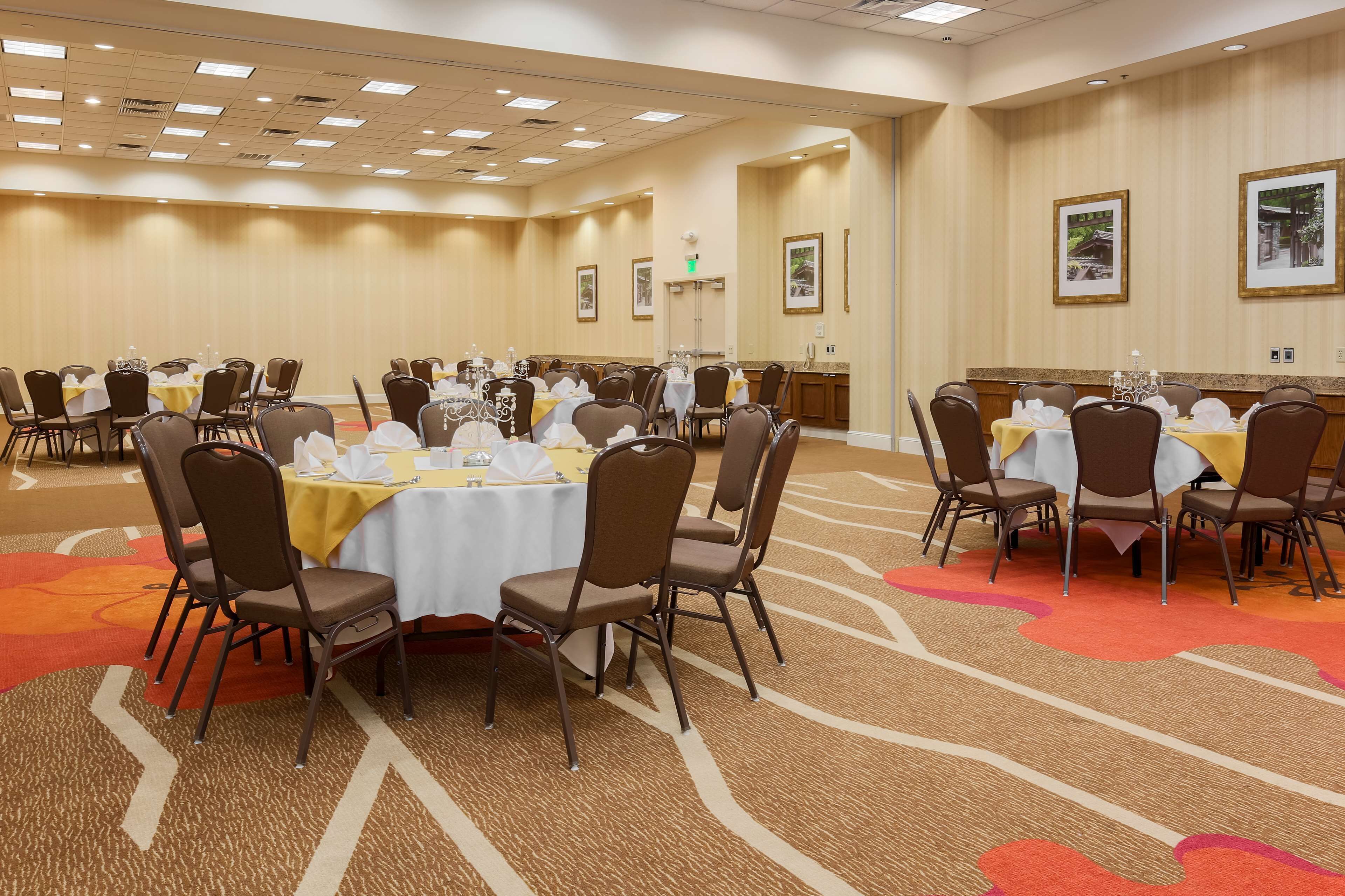 A conference room with multiple tables and chairs, arranged in rows, with a carpeted floor and framed pictures on the walls.