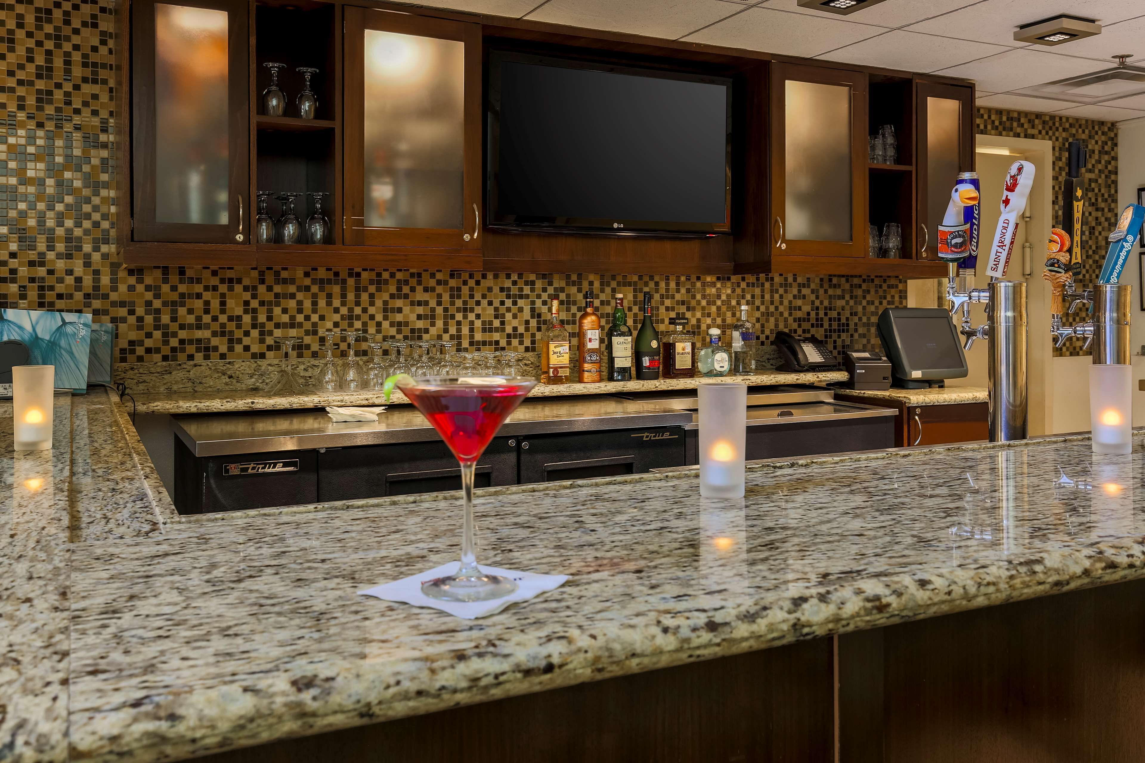 Eine Bar mit einer Granit-Arbeitsplatte, einem Martini-Glas und einem Fernseher über den Schränken.