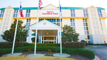 A Hilton Garden Inn with a central entrance, flagpoles, and a well-maintained garden.