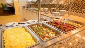 Un buffet proposant une variété de plats, notamment des œufs brouillés, un sauté de légumes et du bacon.