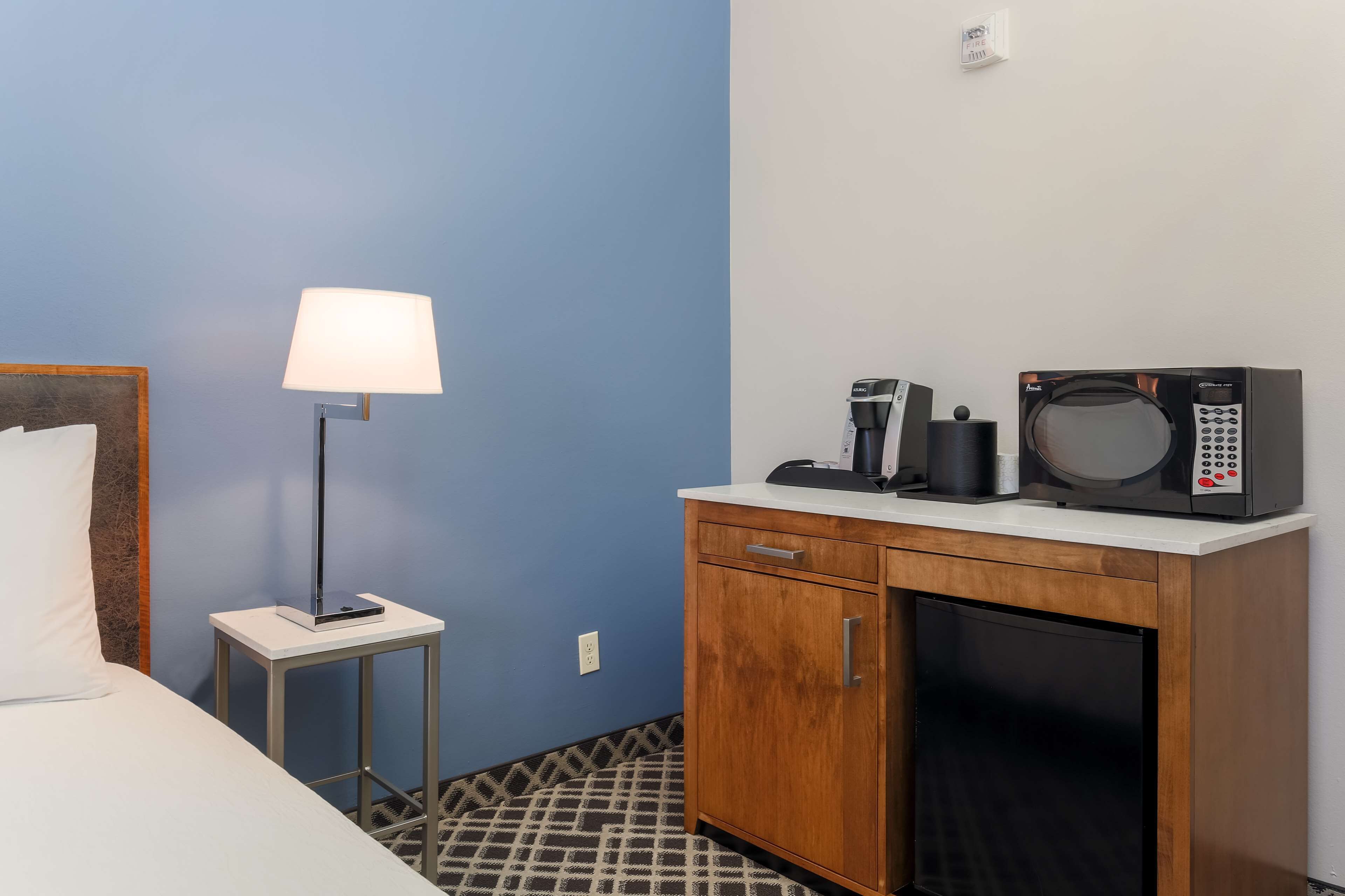 A hotel room with a bed, a bedside lamp, a microwave, and a small cabinet.
