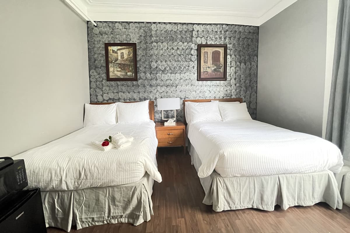 Une chambre d’hôtel avec deux lits simples, une table de chevet en bois, une lampe et un mur décoré de motifs circulaires.