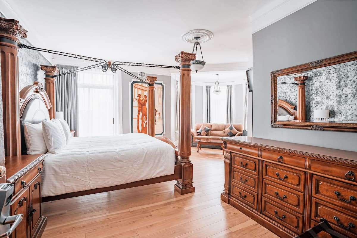 Une chambre spacieuse avec un grand lit, une commode en bois et un lustre classique.