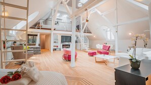 Uma ampla sala em estilo loft, com pé direito alto, escada e varanda.
